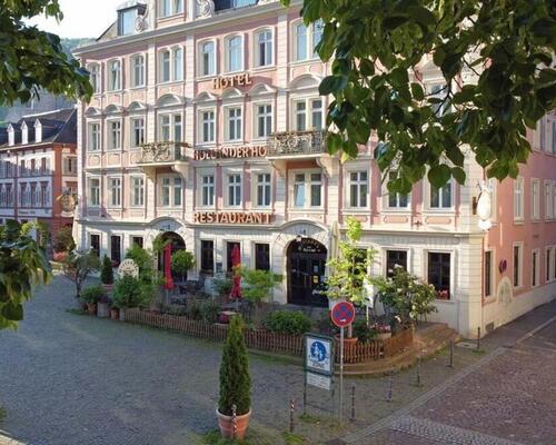 Die prachtvolle rosa Fassade des historischen Hotels Holländer Hof, gesehen durch grüne Blätter, verspricht einen charmanten Aufenthalt.